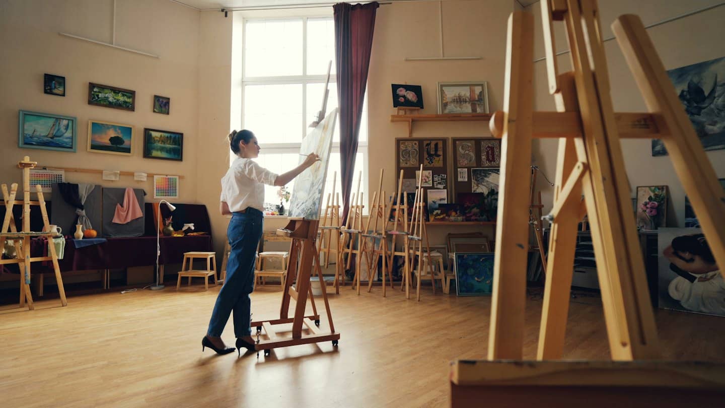 Vrouw schildert een groot doek in een lichte kunststudio.
